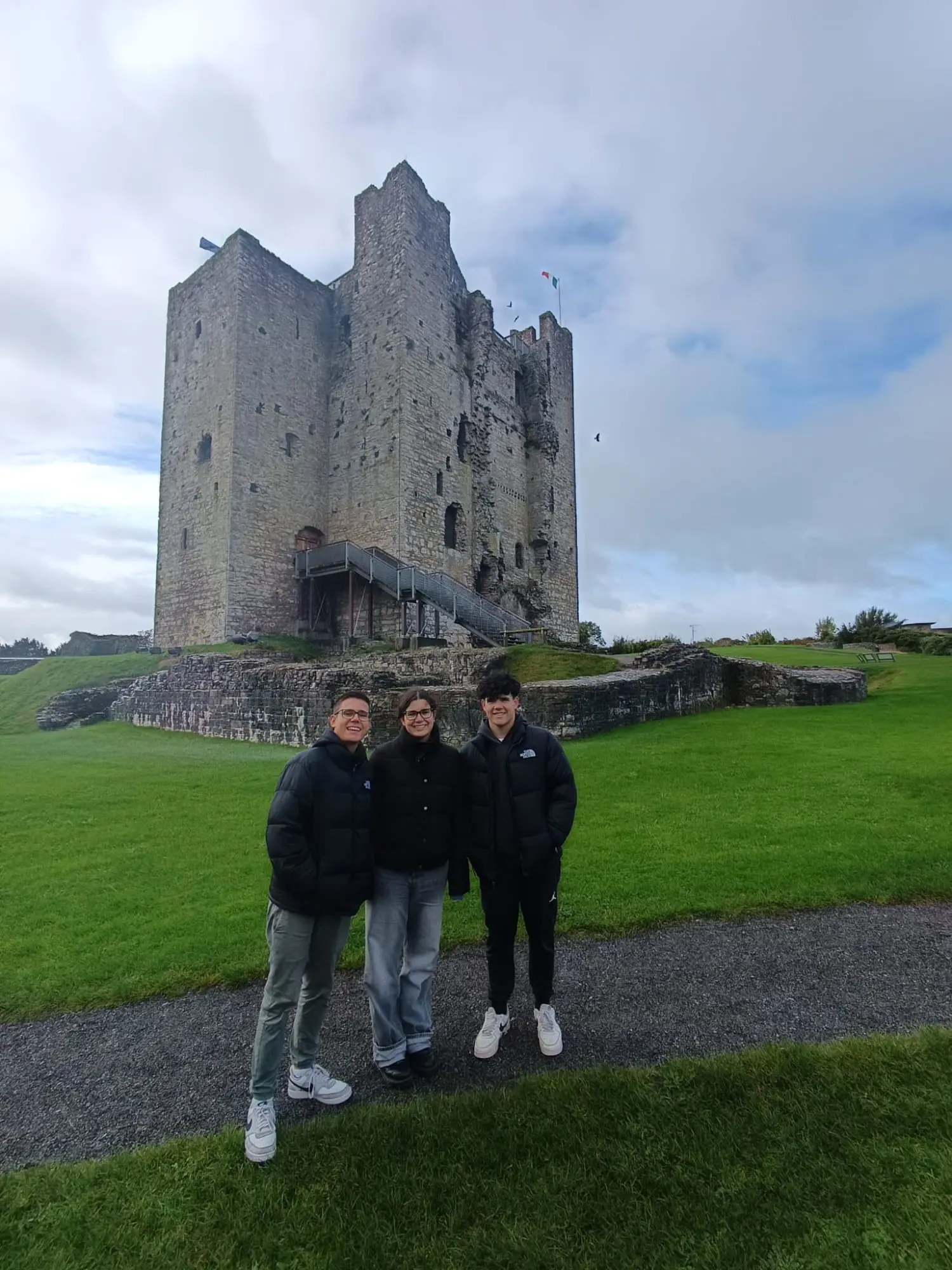 Tres viajeros ante la torre de piedra de un castillo medieval, sobre un prado verde