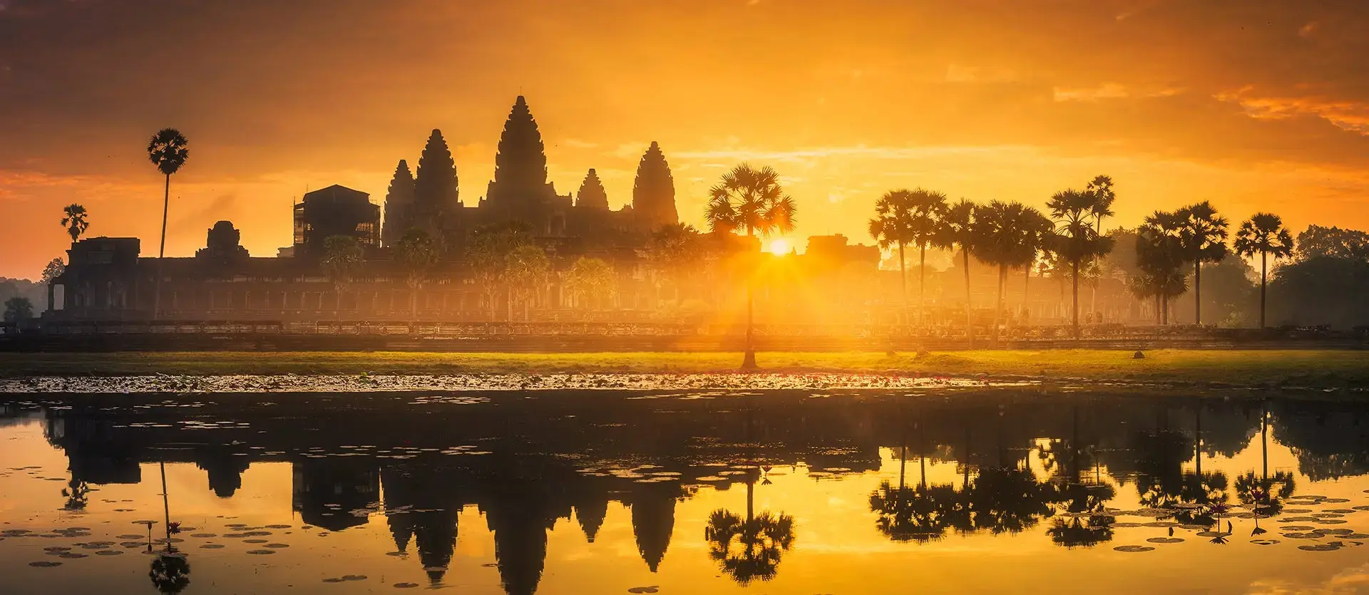 Silueta de Angkor Wat al amanecer reflejada en el estanque, bajo un cielo anaranjado