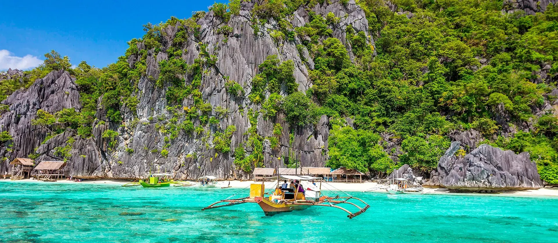 Barca tradicional filipina en aguas turquesas frente a acantilados de piedra caliza cubiertos de vegetación