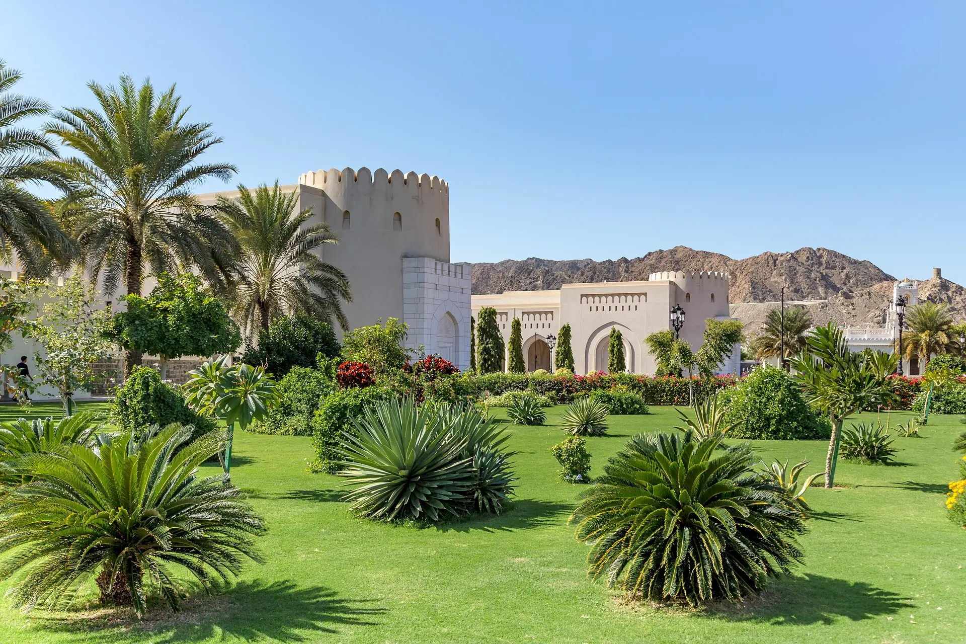 Fortaleza de muros claros entre palmeras y jardines, con montañas áridas al fondo, en Omán