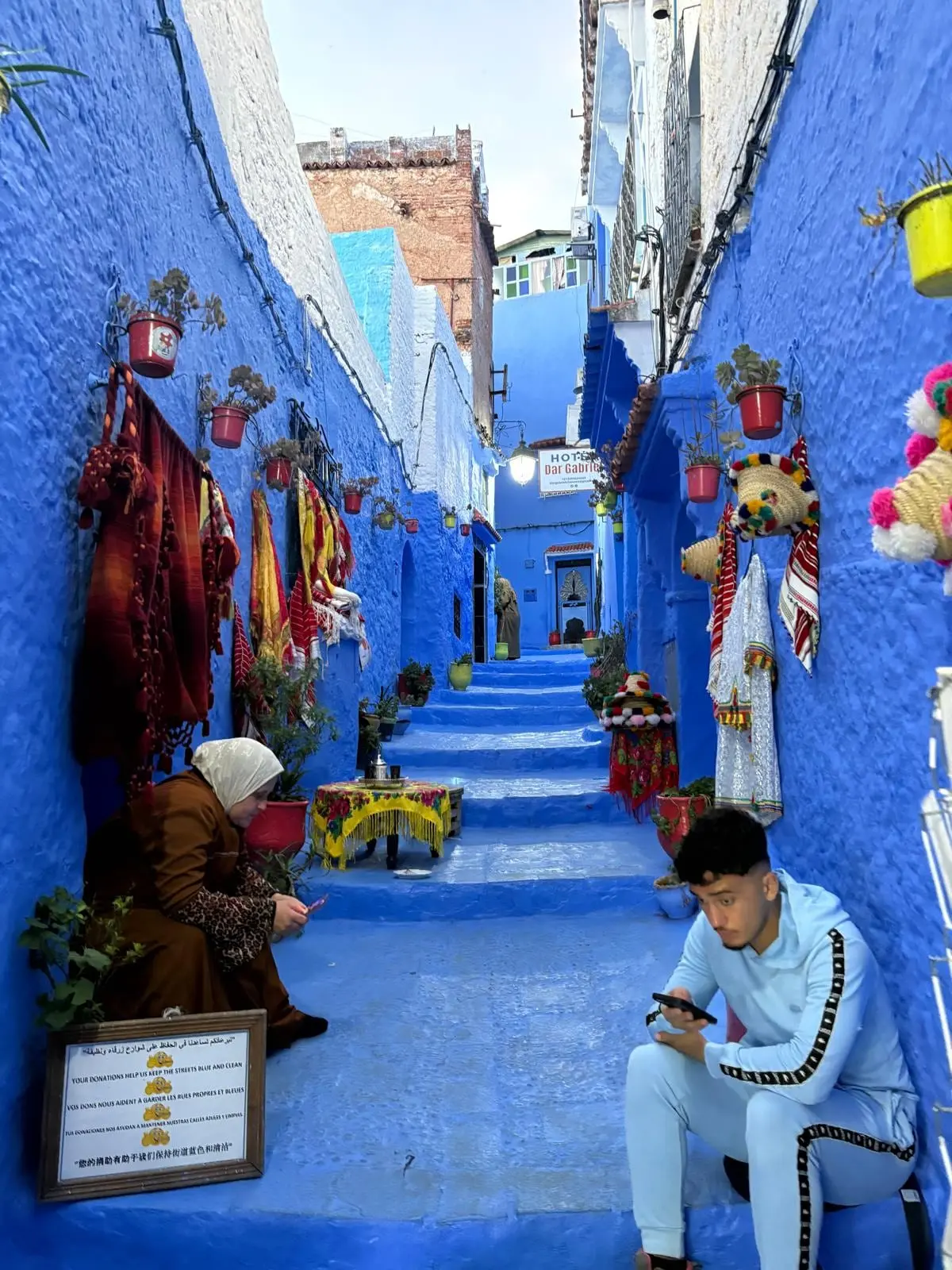 Callejuela azul de Chefchaouen (Marruecos) con puestos de artesanía y vecinos sentados en los escalones