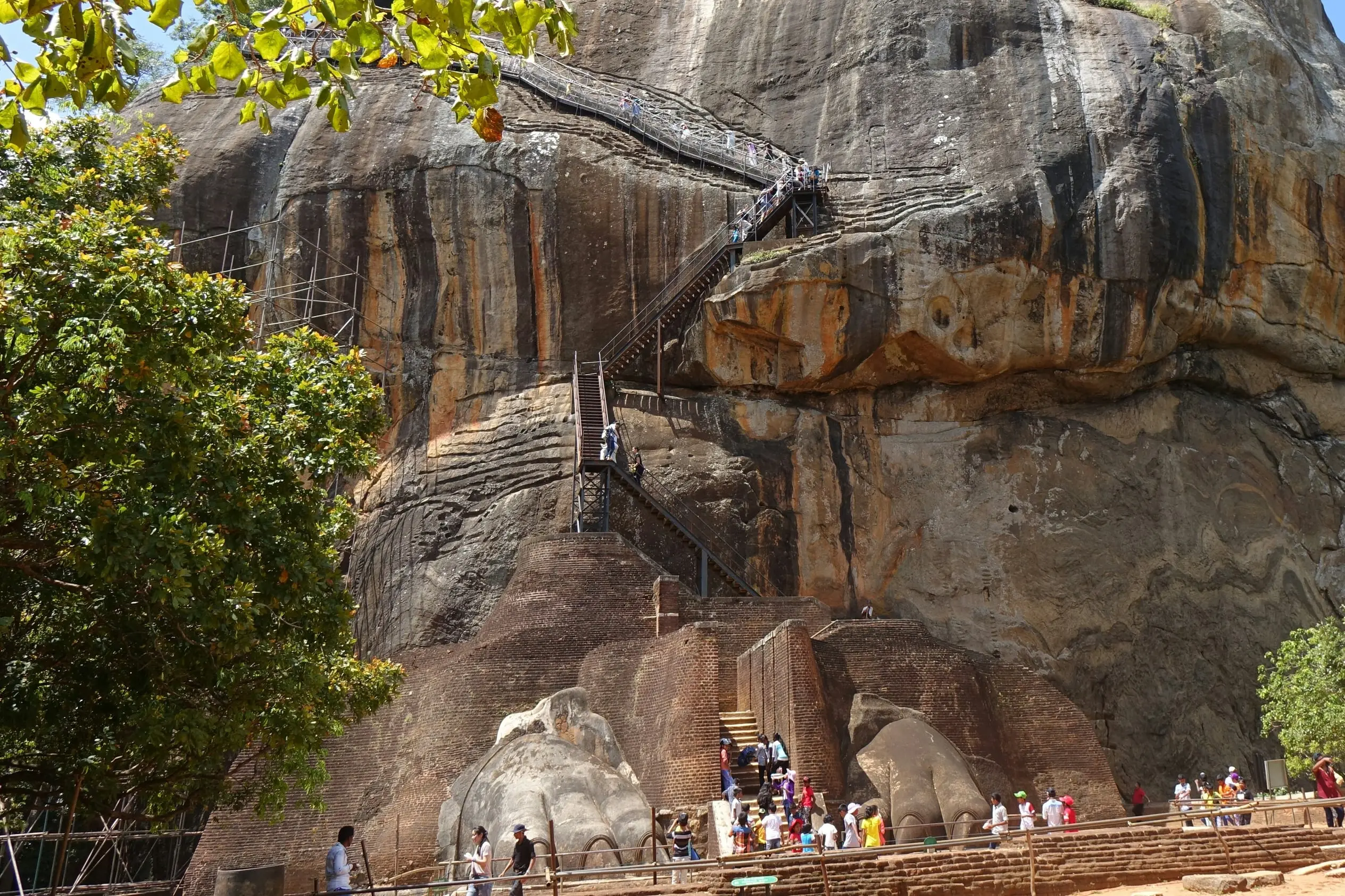 Visitantes subiendo por la escalinata entre las garras de león de la Roca de Sigiriya y por las escaleras metálicas que trepan por la roca